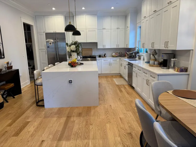 White kitchen with a quartz island, stainless steel appliances and clean hardwood floors