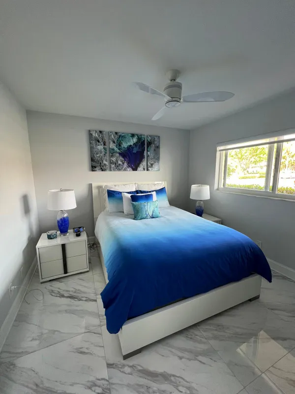 Bedroom with a blue and white bed, white nightstands and a polished marble-look floor